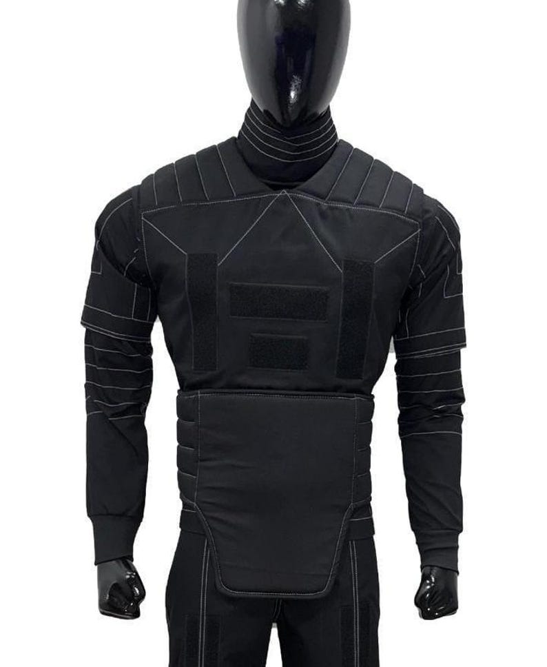 May include: Black tactical vest with white stitching details, displayed on a mannequin. The vest features multiple panels, hook-and-loop closures, and long sleeves. The mannequin is wearing a black turtleneck and pants.