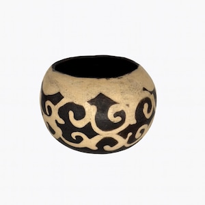 May include: A round, handcrafted ceramic bowl with a black interior and a cream-colored exterior. The exterior features a repeating pattern of black, swirling, abstract shapes. The bowl is set against a white background.