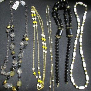 May include: Selection of necklaces in diverse styles. Features beaded, chain, and pendant designs. Colours include black, white, yellow, gold, and clear. Some necklaces have tags attached.