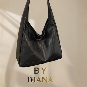 Può includere: Una borsa hobo nera con un design patchwork, cuciture visibili e un unico tracolla. Il testo BY DIANA è stampato in lettere dorate sotto la borsa. La borsa presenta una finitura liscia e opaca con una forma morbida e destrutturata.