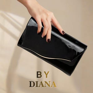 May include: A black patent leather clutch bag with a glossy finish and a curved flap edge. The bag features a thin gold-toned metallic accent along the closure. The text BY DIANA is printed in gold lettering below the clutch bag.