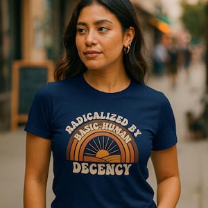 May include: Navy blue t-shirt with the text "RADICALIZED BY BASIC-HUMAN DECENCY" in a retro design featuring a rainbow and sun graphic. The shirt is short-sleeved.