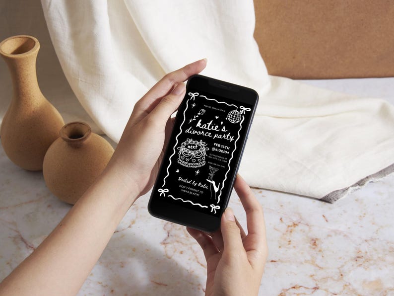 May include: A black smartphone displays a white invitation for "Katie's divorce party." The invitation includes a cake, disco ball, and martini glass illustrations. The text reads "Feb 14th 06:00PM" and "Don't forget to wear black."