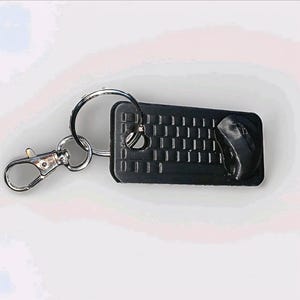 May include: A black keyboard and mouse keychain with a silver key ring and clasp. The keyboard has a detailed key layout, and the mouse is positioned to the right. The keychain is a fun accessory for tech enthusiasts.
