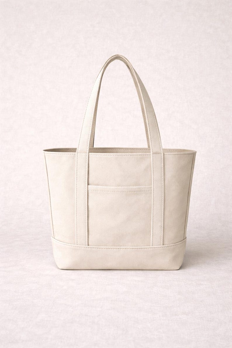 K&ouml;nnte beinhalten: Cremefarbene Tragetasche mit rechteckiger Form und zwei Griffen. Die Tasche hat eine Vordertasche und verst&auml;rkte N&auml;hte. Die neutrale Farbe und das schlichte Design machen sie zu einem vielseitigen Accessoire.