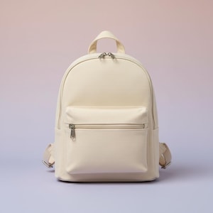 May include: Cream-colored backpack with a front zippered pocket and a top handle. The backpack has adjustable shoulder straps and silver-toned hardware. The bag is made of a canvas-like material and is set against a soft, gradient background.