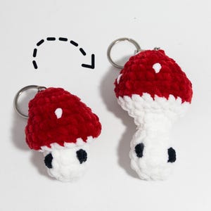May include: Two handmade mushroom keychains. The mushroom caps are red with white spots, and the stems are white with black accents. The keychains are made of a soft, textured material and have silver key rings.
