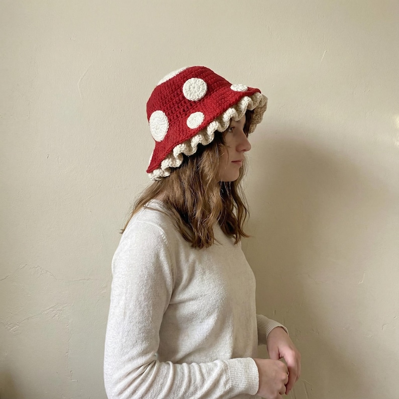 May include: A handmade red crochet bucket hat with white polka dots and a scalloped brim. The hat is a whimsical accessory, perfect for adding a touch of fun to any outfit. The hat's brim is approximately 3 inches wide.