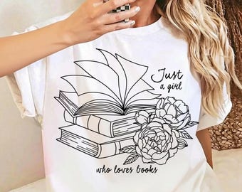 May include: A white t-shirt featuring a black line art graphic of a stack of books with an open book on top and floral accents. The text "Just a girl who loves books" is printed in a black script font around the central book and flower illustration.