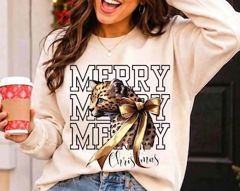May include: A cream-colored long-sleeve sweatshirt featuring a graphic of a leopard cub wearing a large gold bow. The text "MERRY MERRY MERRY" is printed in a black collegiate font behind the cub, with the word "Christmas" in script below.