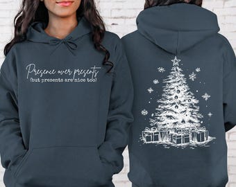 May include: A dark slate blue hooded sweatshirt featuring white text on the front that reads Presence over presents (but presents are nice too). The back displays a white line art graphic of a decorated Christmas tree with gifts.