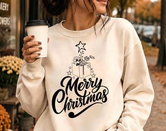 May include: A cream-colored crewneck sweatshirt featuring a black graphic print. The design includes an open book with flowers, a star above it, and the text Merry Christmas in a bold, cursive script. The sweatshirt has long sleeves and ribbed cuffs.