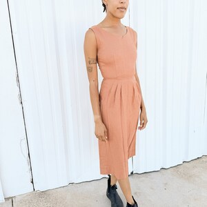 May include: A woman wearing a terracotta midi dress with a sleeveless design and a scoop neck. She is wearing black ankle boots and a white patterned headband.
