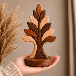 May include: A decorative wooden tree sculpture featuring a symmetrical arrangement of leaves in alternating light and dark brown wood tones. The tree stands on a circular wooden base, showcasing smooth, polished surfaces and distinct wood grain patterns.