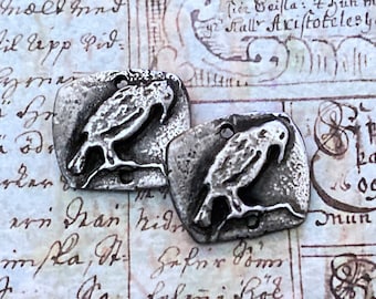 May include: Two silver-toned metal charms shaped like a bird perched on a branch. The charms have a rustic, antique finish.
