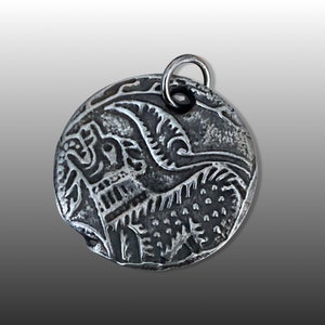 May include: A silver pendant with an intricate design of a bird with its wings spread. The pendant is round and has a loop at the top for attaching a chain.