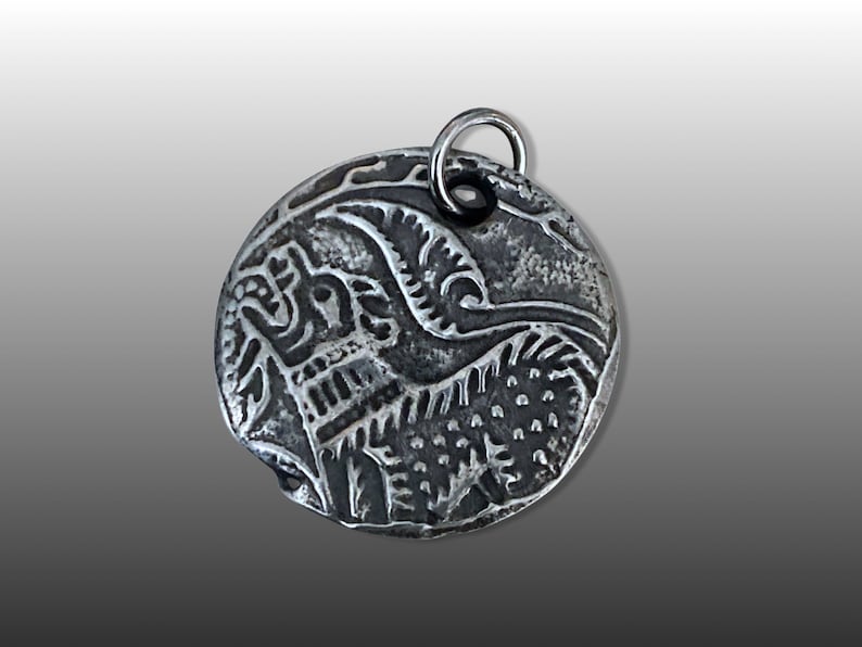 May include: A silver pendant with an intricate design of a bird with its wings spread. The pendant is round and has a loop at the top for attaching a chain.
