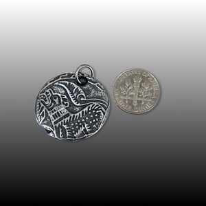 May include: A silver pendant with an intricate design of a bird in flight. The pendant is about the size of a US dime.