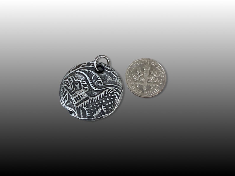 May include: A silver pendant with an intricate design of a bird in flight. The pendant is about the size of a US dime.