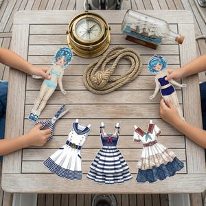 Nautical Sailor style paper doll with navy blue outfits and anchor accessories on a desk. Features a 16cm tall doll with pre-fitted marine fashion. High-resolution printable PDF for creative play and scrapbooking. Part of a 120-page mega bundle inspired by modern Pinterest aesthetics.