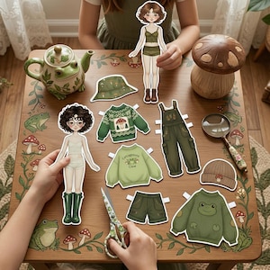 Frogcore aesthetic paper doll set spread on a workspace. Includes green cottagecore-style clothing, mushroom accessories, and a 16cm tall doll. Real dried leaves and a small ceramic frog on the table. Perfect for nature-inspired mood boards, creative play, and green-themed scrapbooks.