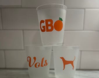May include: Three clear plastic cups stacked on top of each other. The top cup has the letters "GBO" and an orange graphic. The middle cup says "Vols" in orange lettering. The bottom cup has an orange dog silhouette.