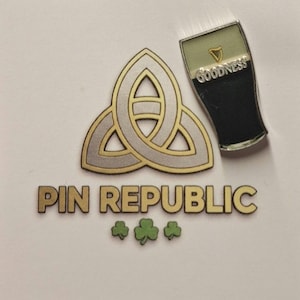 Puede incluir: Colección de pines con un diseño de nudo celta dorado y plateado, una pinta de Guinness con la palabra "Goodness" y el texto "PIN REPUBLIC" con tres tréboles verdes. Los pines están sobre un fondo blanco.