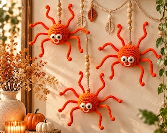 May include: Three bright orange crocheted spiders with large white eyes and smiling mouths, each suspended from a vertical string of wooden beads. The spiders feature eight long, curled legs and are arranged in a decorative hanging display.