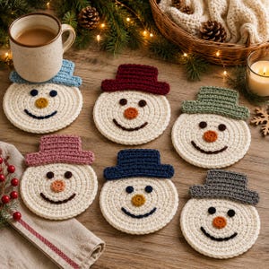 May include: A set of six round, cream-colored crocheted snowman coasters, each featuring a different colored hat in light blue, dark red, sage green, dusty pink, navy blue, and gray, with dark eyes, an orange nose, and a dark smile.