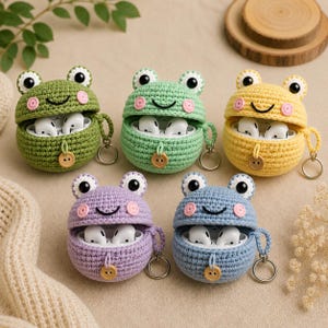 Puede incluir: Cinco fundas de ganchillo para auriculares con forma de rana en verde oliva, verde claro, amarillo, lavanda y azul. Cada funda tiene dos ojos, mejillas rosas, una sonrisa bordada, un botón de madera y una anilla metálica.