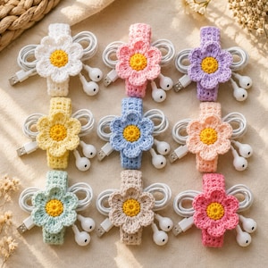 May include: Nine crochet cable organizers arranged in a grid, each featuring a different colored flower with a yellow center. The colors include white, pink, purple, yellow, blue, peach, light green, beige, and dark pink, all securing white cables.