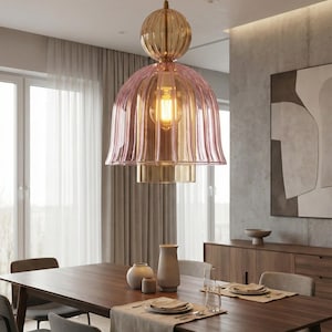 Könnte beinhalten: Ein modernes Esszimmer mit einem großen Holztisch und Stühlen. Über dem Tisch hängt eine dekorative Pendelleuchte. Die Leuchte hat einen rosafarbenen Glasschirm und eine goldfarbene Oberseite. Der Raum hat neutrale Farben und ein minimalistisches Design.