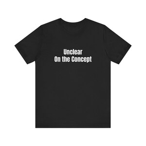 以下が含まれることがあります： 胸の中央にサンセリフ体の白い文字で「Unclear On the Concept」とプリントされた、黒の半袖Tシャツ。この衣類は、クラシックなクルーネックと標準的なストレートカットのシルエットが特徴です。
