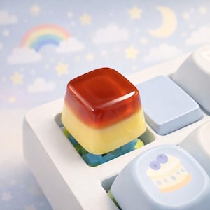 May include: A custom keyboard keycap with a layered design. The top layer is a translucent reddish-brown, transitioning to yellow, and set on a white keyboard. The background features a rainbow, clouds, stars, and a crescent moon.