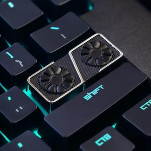 May include: Close-up of a black keyboard with teal illuminated keys. The Shift key is visible, along with a custom keycap featuring a dual fan design. The keyboard has a modern, tech-focused aesthetic.