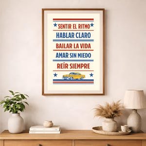May include: Framed art print with the words "SENTIR EL RITMO, HABLAR CLARO, BAILAR LA VIDA, AMAR SIN MIEDO, REÍR SIEMPRE" in red and blue stripes. A yellow car graphic is at the bottom. The print is in a wooden frame.