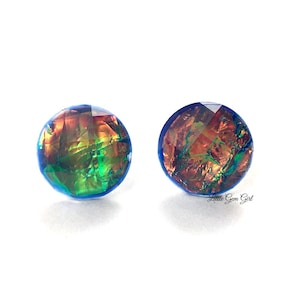 Peut inclure: Une paire de boucles d'oreilles clous irisées bleu et vert avec un reflet cuivré et doré. Les boucles d'oreilles sont rondes et ont une bordure bleue.