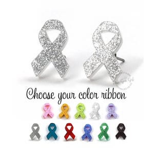 Op de afbeelding: Twee zilveren glitter oorknopjes in de vorm van een bewustwordingslintje boven de tekst "Choose your color ribbon" en een overzicht van vijftien kleine lintbedels in diverse kleuren zoals roze, oranje, limoengroen, wit, paars, grijs, teal, rood, blauw, groen en zwart.