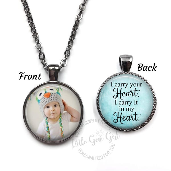 May include: A silver necklace with a round glass pendant. The front of the pendant has a photo of a baby wearing a hat. The back of the pendant has the text "I carry your Heart. I carry it in my Heart."