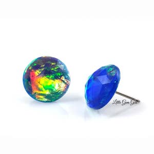 May include: A pair of iridescent opal earrings with a blue and green colour scheme. The earrings are set in a round shape and have a silver post.