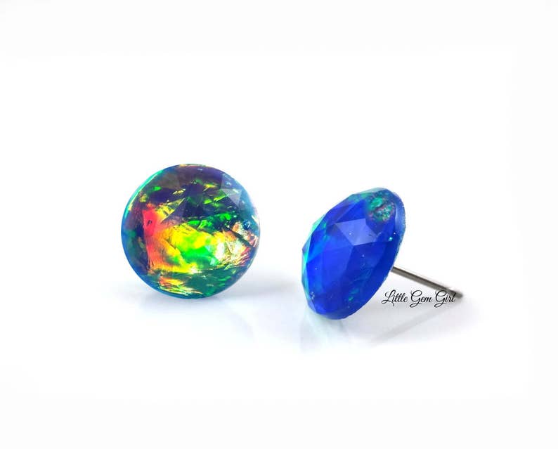 May include: A pair of iridescent opal earrings with a blue and green colour scheme. The earrings are set in a round shape and have a silver post.