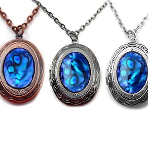 Op de afbeelding: Drie ovale hangers met blauwe abalone-schelpincrustaties. De hangers zijn aan zilveren, koperen en antieke zilveren kettingen.
