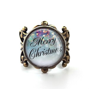 May include: A bronze ring with a round glass cabochon featuring a snowy scene with colorful lights and the text "Merry Christmas".