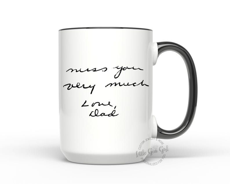 Może przedstawiać: Biały ceramiczny kubek z czarną obw&oacute;dką i uchwytem. Kubek zawiera odręczny tekst, kt&oacute;ry brzmi "miss you very much Love, Dad". Kubek to spersonalizowany prezent.