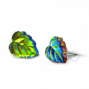 Op de afbeelding: Een paar oorringen van iriserend glas in de vorm van een blad. De bladeren zijn groen, blauw en rood met een metallic glans. De oorringen zijn een uniek en stijlvol accessoire.
