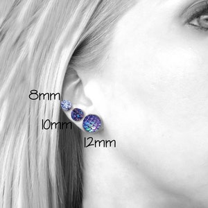 Pu&ograve; includere: Riferimento di dimensioni per gli orecchini. Tre paia di orecchini sono mostrati sull'orecchio di una persona. Gli orecchini hanno un diametro di 8 mm, 10 mm e 12 mm. Gli orecchini sono viola e iridescenti.