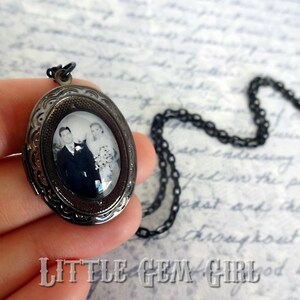 May include: A black metal locket necklace with a black and white photograph of a couple inside. The locket has an intricate design and a chain.
