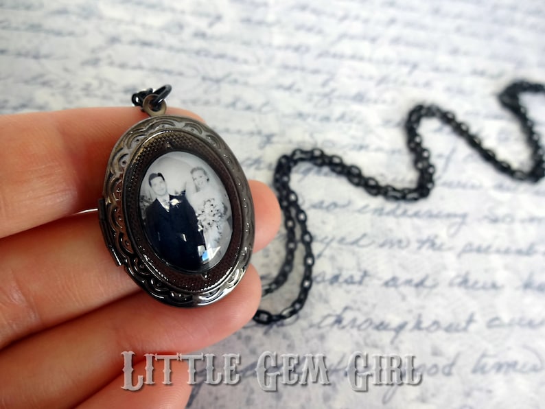 May include: A black metal locket necklace with a black and white photograph of a couple inside. The locket has an intricate design and a chain.