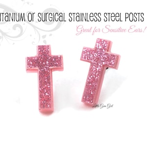May include: A pair of pink glitter cross earrings with titanium or surgical stainless steel posts. The earrings are labeled "Great for Sensitive Ears!"