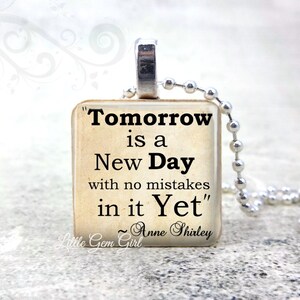 May include: A square pendant necklace featuring the quote "Tomorrow is a New Day with no mistakes in it Yet" by Anne Shirley. The pendant has a silver bail and hangs on a silver ball chain. The background is a soft, blurred white.